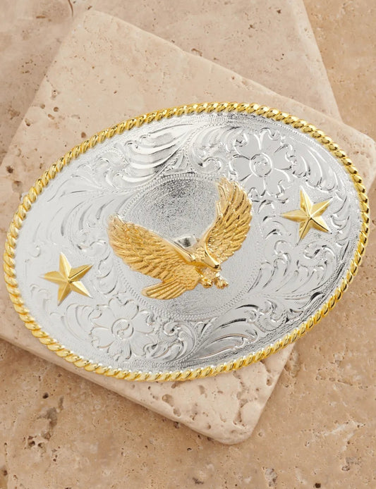 Silver and gold belt buckle with eagle design on a beige stone background