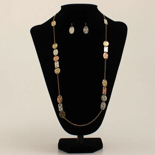 Jewelry set with necklace and earrings made of various hammered metals in oval and square shapes, on a black stand against a beige background