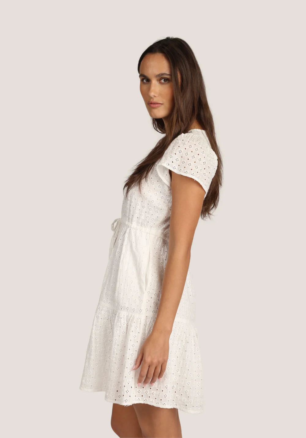 Side view of woman wearing a white lace dress against a plain background