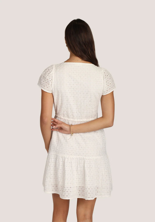 Back view of a woman wearing a white dress with lace details on a plain background