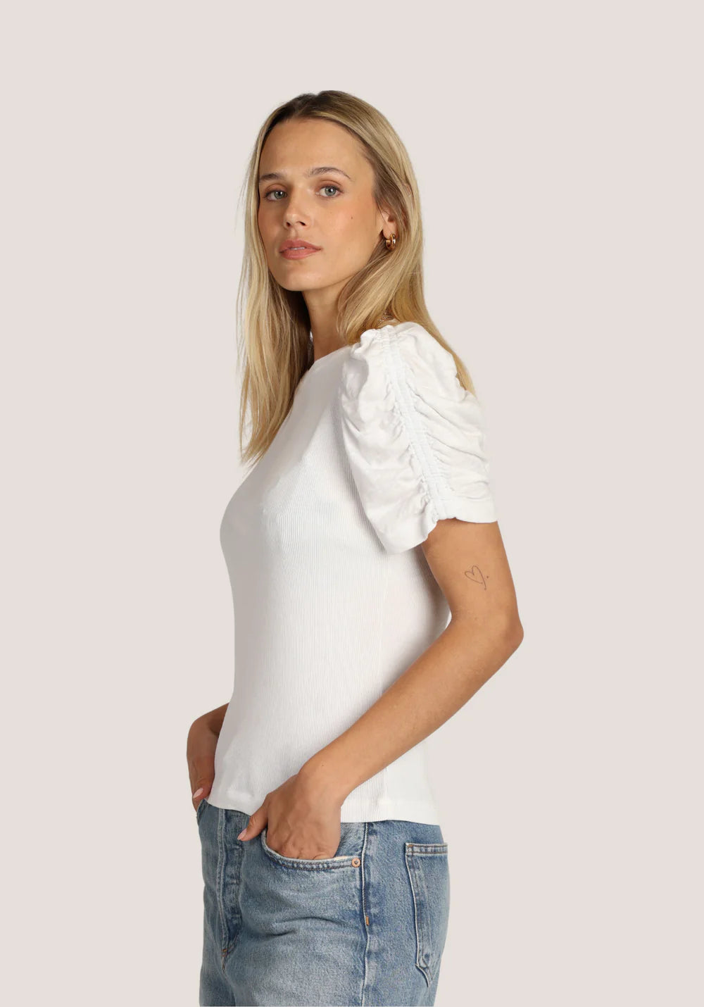 Side view of a woman wearing a white blouse with puffed sleeves and blue jeans on a plain background
