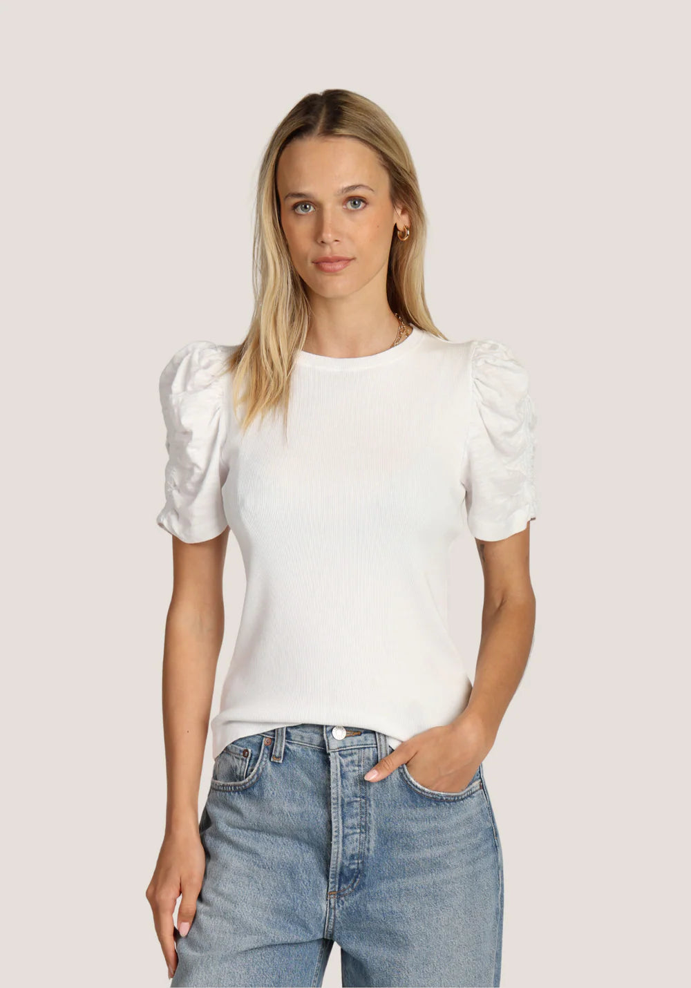 Woman wearing a white blouse with puff sleeves and blue jeans on a light pink background