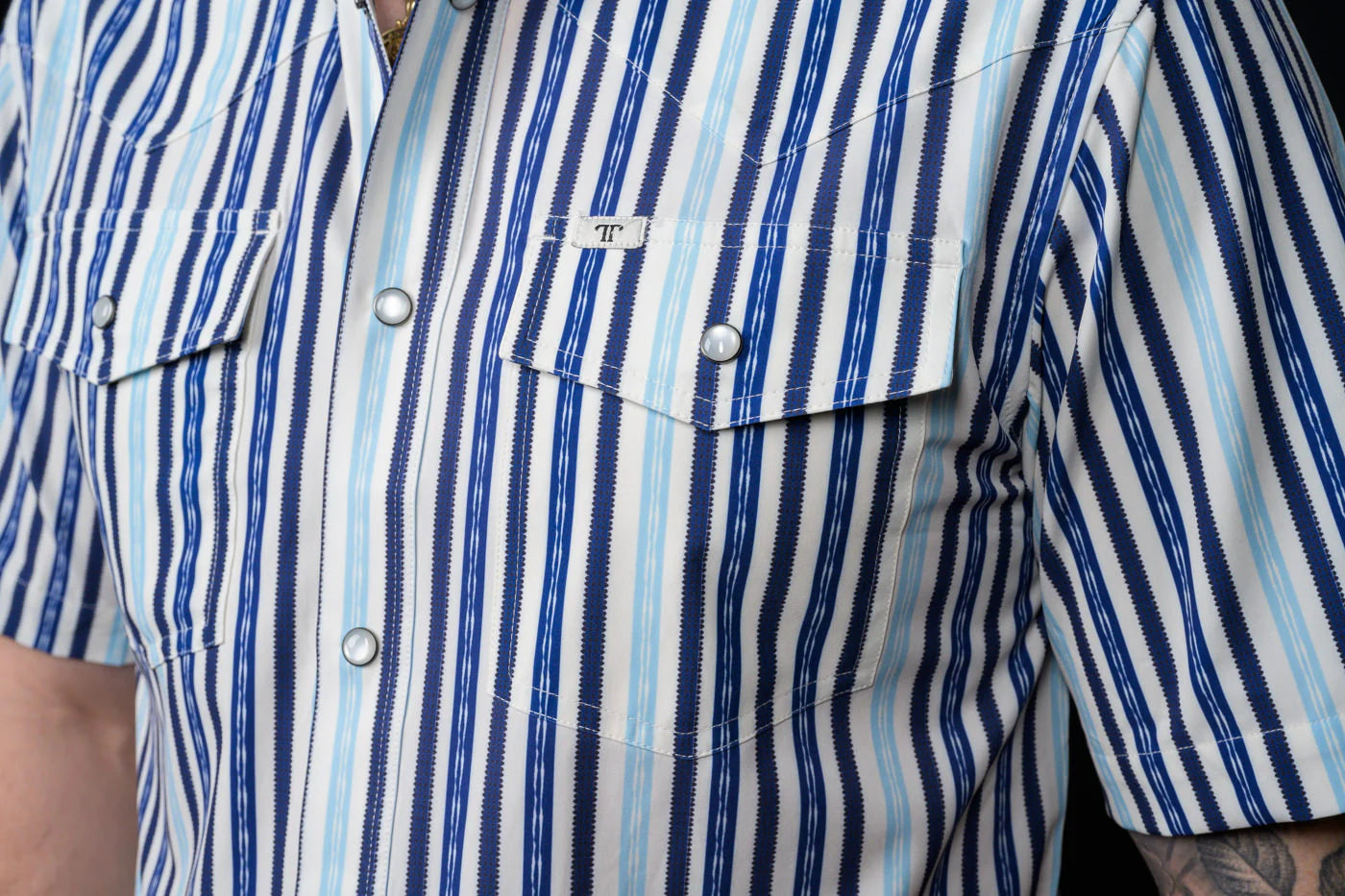 Close-up of a person wearing a blue and white striped, pearl snap shirt with a Ferrell Brand logo.