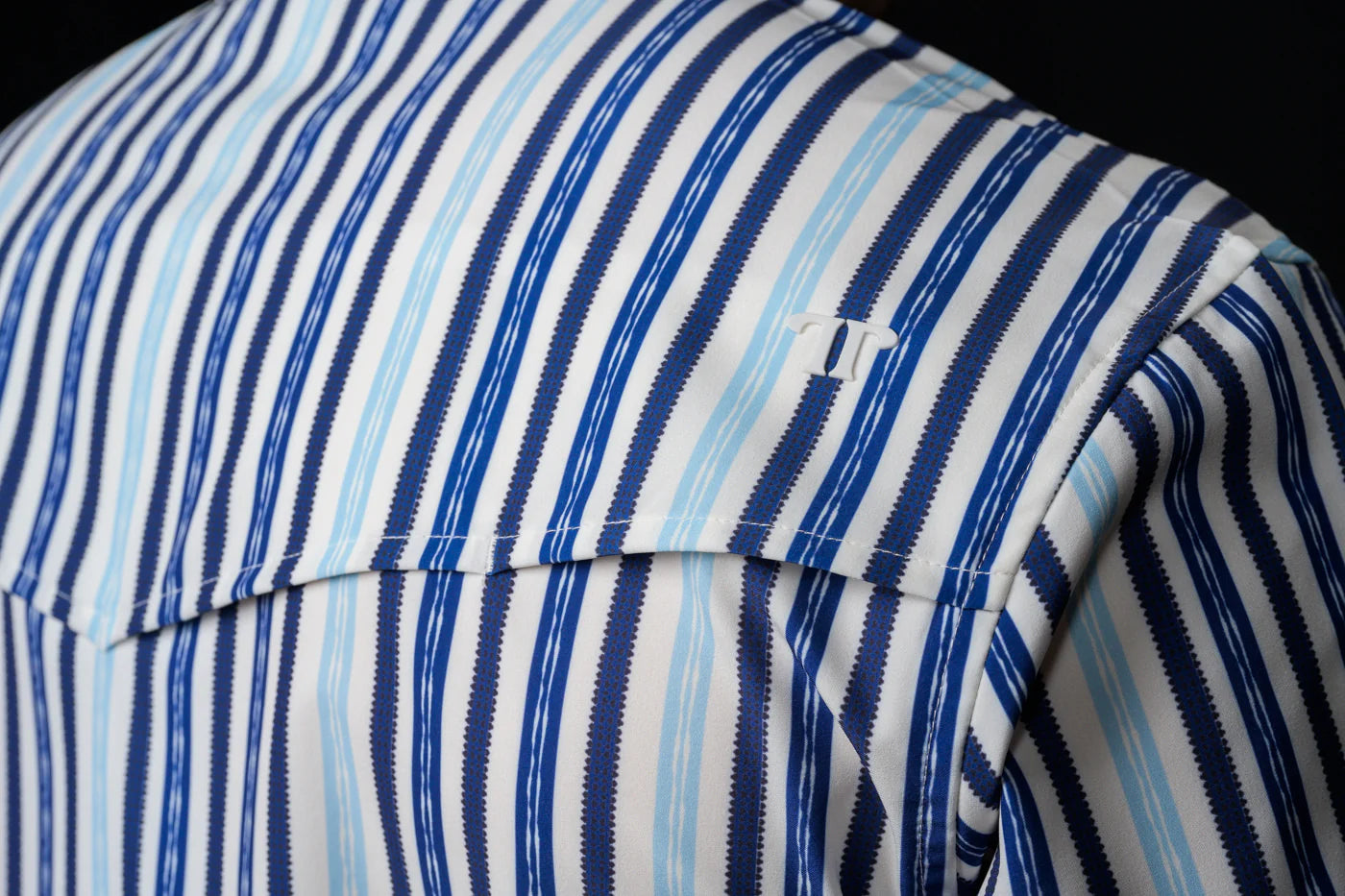 Close-up of the back yoke of blue and white striped, Ferrell Brand shirt with a black background