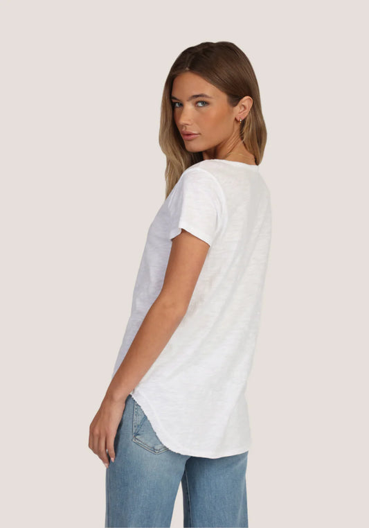 Side/ Back view of a woman wearing a white t-shirt and blue jeans on a light cream background