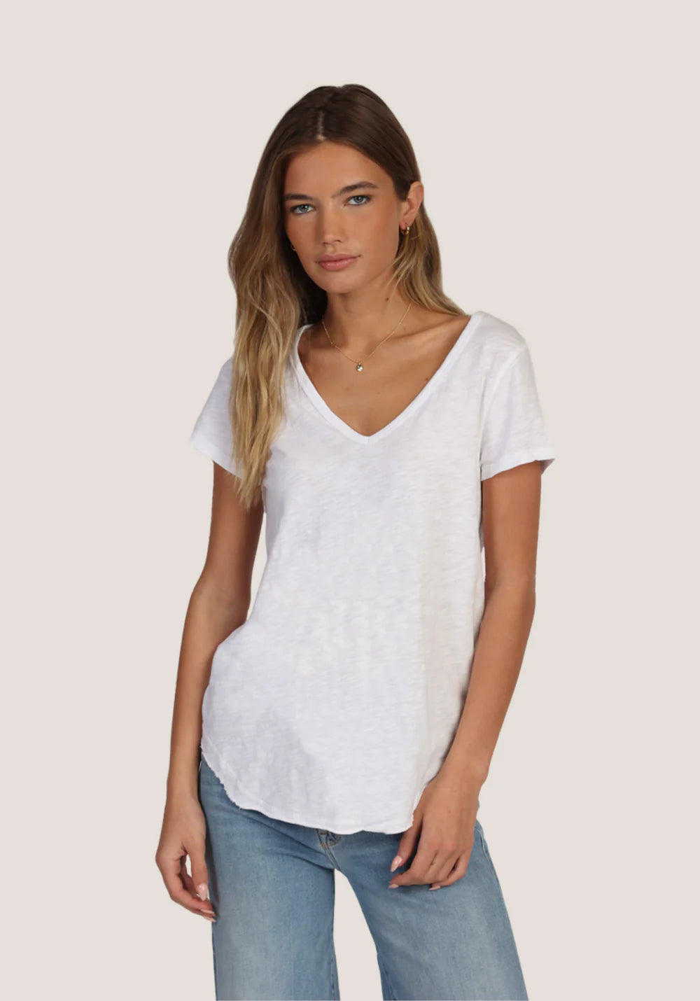 Woman wearing a white, V-Neck t-shirt and blue jeans against a plain background