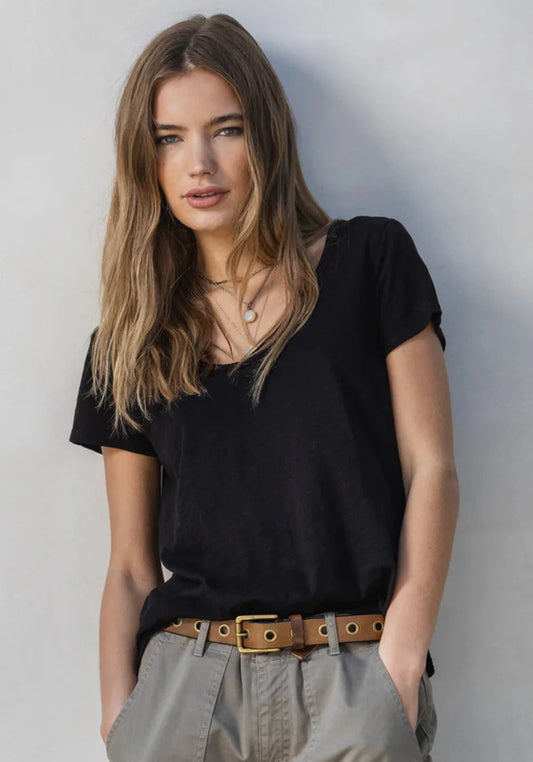 Woman wearing a black, V-neck t-shirt and beige pants against a gray background