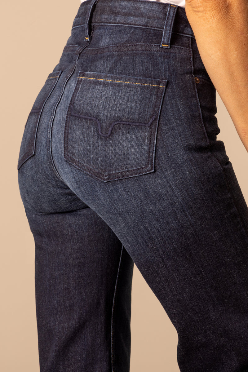 Close up of the back pockets of high waisted and dark washed Kimes Olivia flared jeans against a beige wall.