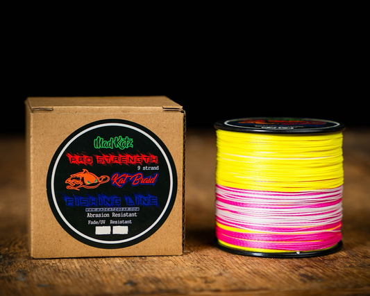 Spool of yellow and pink fishing line next to a cardboard box with Mad Katz branding on a wooden surface.
