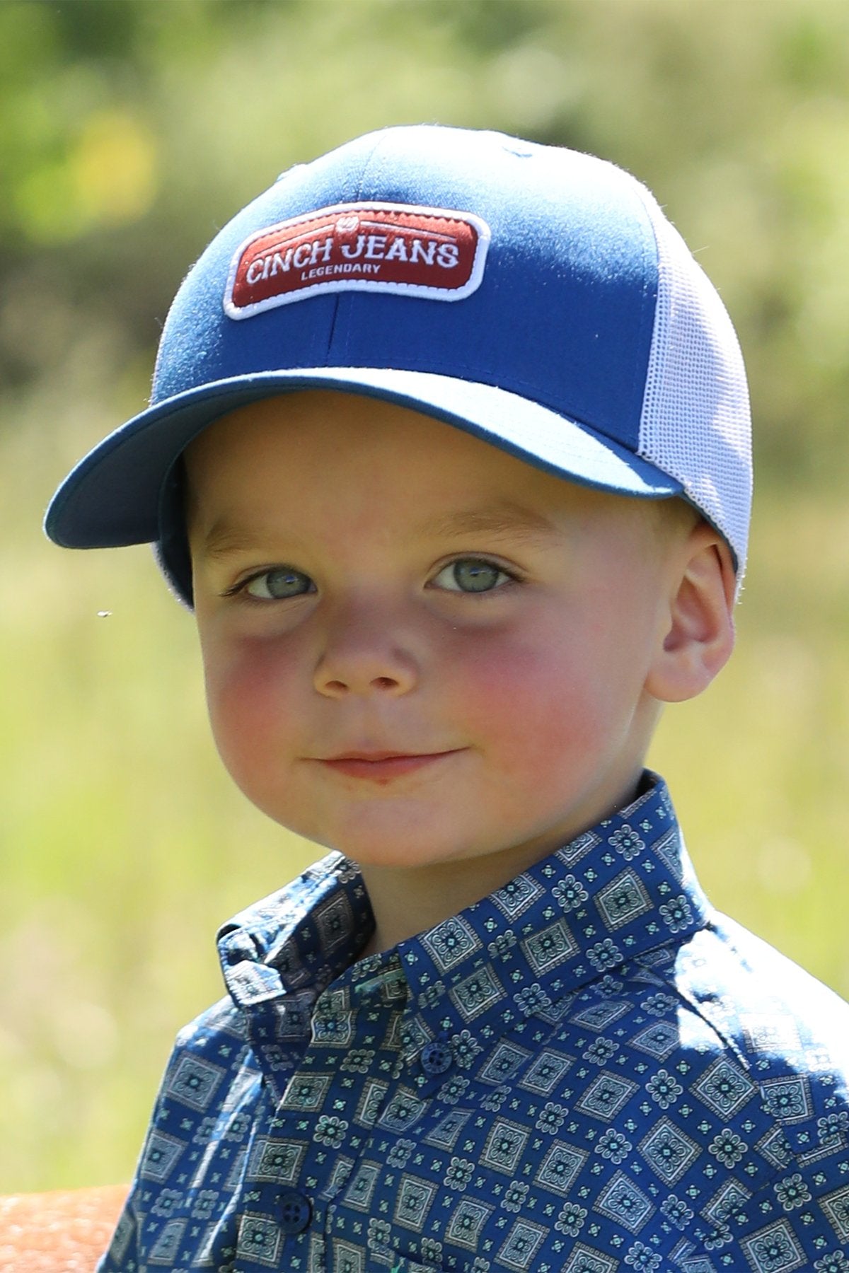 Young boy, outside, wearing royal blue Cinch Jeans trucker cap