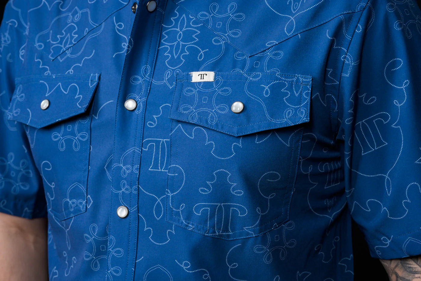 Close-up of a blue patterned, pearl snap shirt with a Ferrell Brand logo.