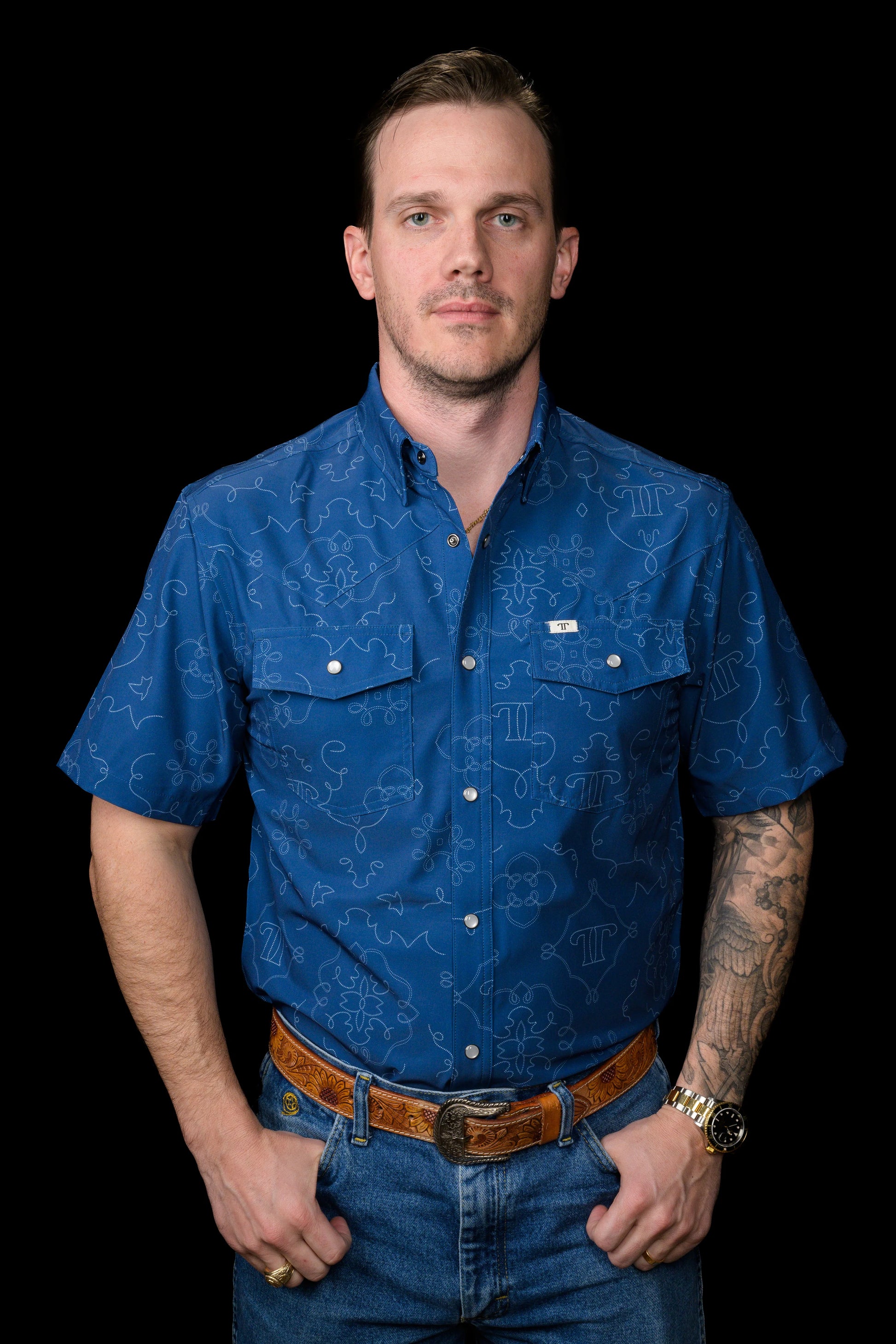 Man wearing a blue patterned Ferrell Brand shirt and jeans on a black background