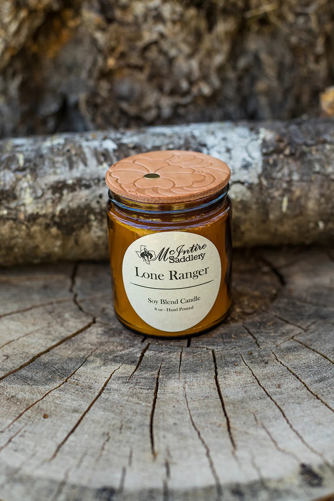 Jar of 'Lone Ranger' candle by McIntire Saddlery on a wooden surface with a log in the background.
