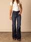 Woman wearing high waisted and dark washed Kimes Olivia flared jeans and a white t-shirt against a beige wall.