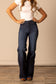 Woman wearing high waisted and dark washed Kimes Olivia flared jeans and a white t-shirt against a beige wall.