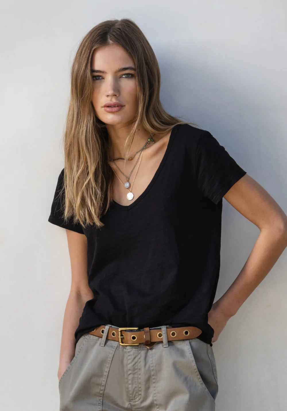 Woman wearing a black V-neck t-shirt and beige pants against a plain background