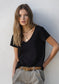 Woman wearing a black V-neck t-shirt and beige pants against a plain background
