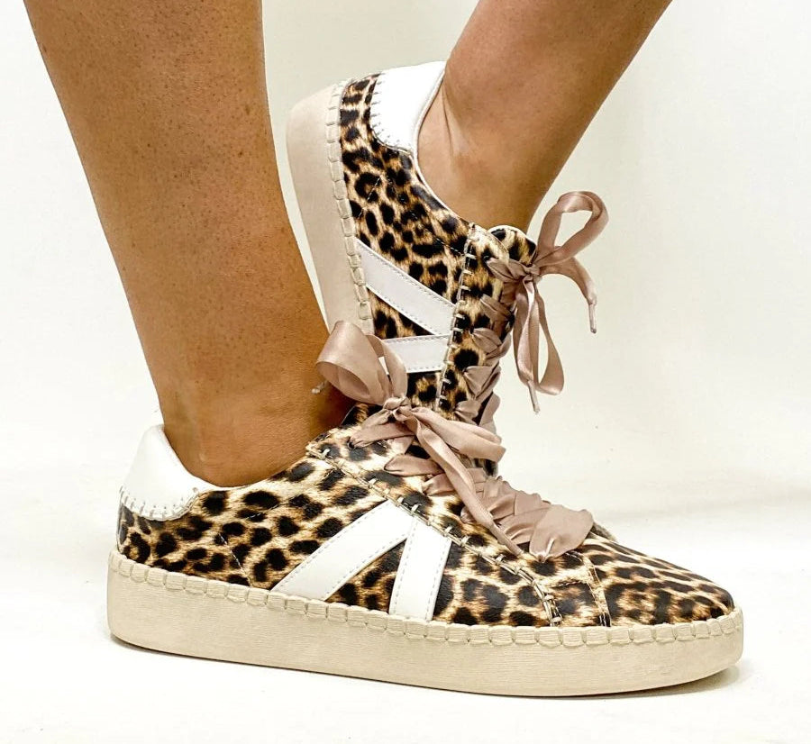 Leopard print sneakers with pink ribbon laces worn by a person on a white background