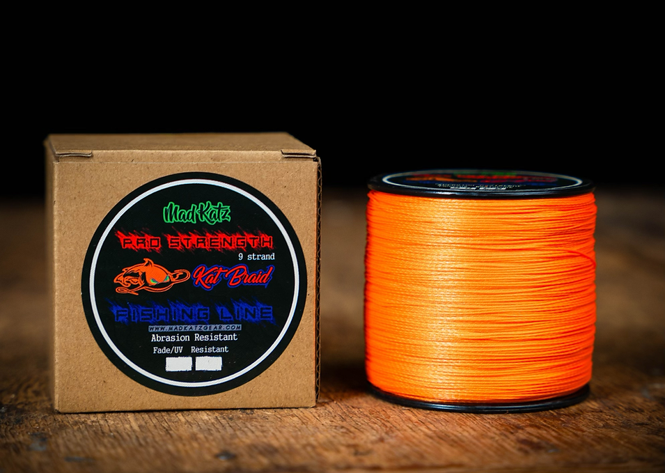 Spool of orange fishing line next to its packaging on a wooden surface
