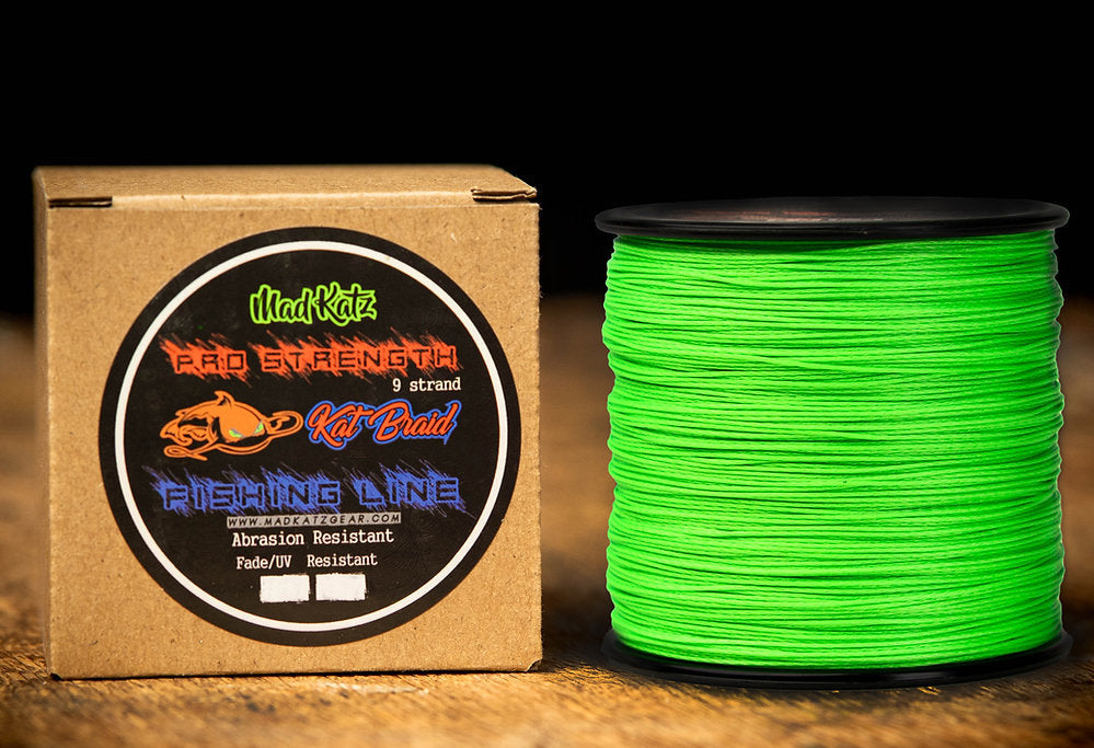 Green spool of fishing line next to a cardboard box with Mad Katz branding on a wooden surface.