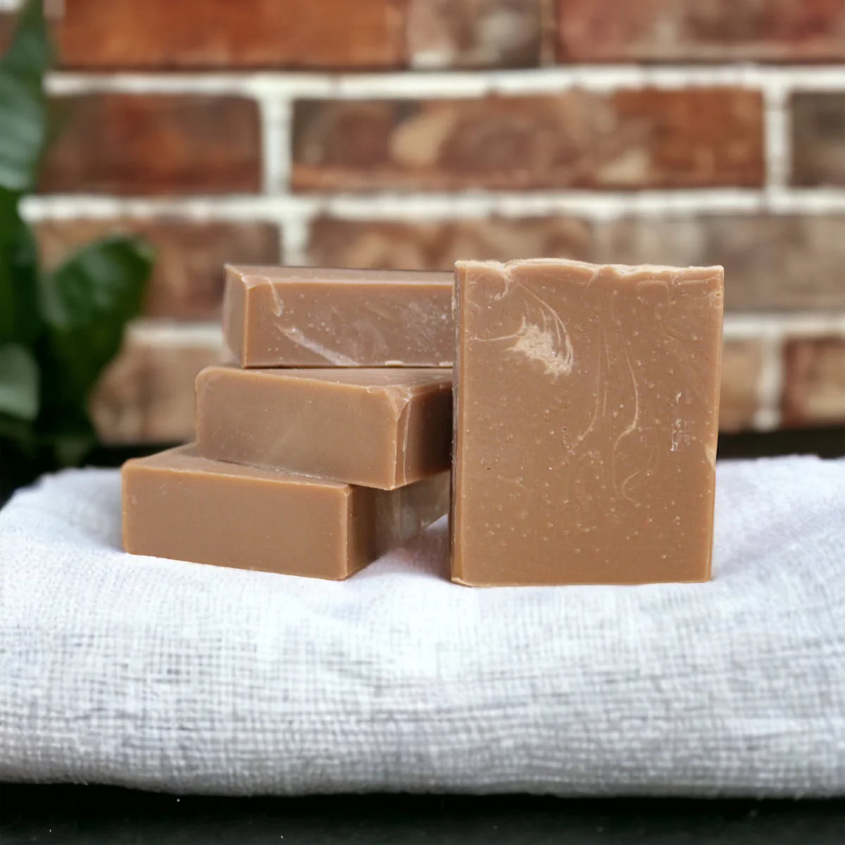 Four bars of brown soap stacked on a white cloth with a brick wall background