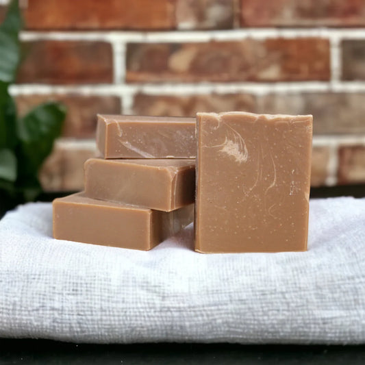 Four bars of brown soap stacked on a white cloth with a brick wall background