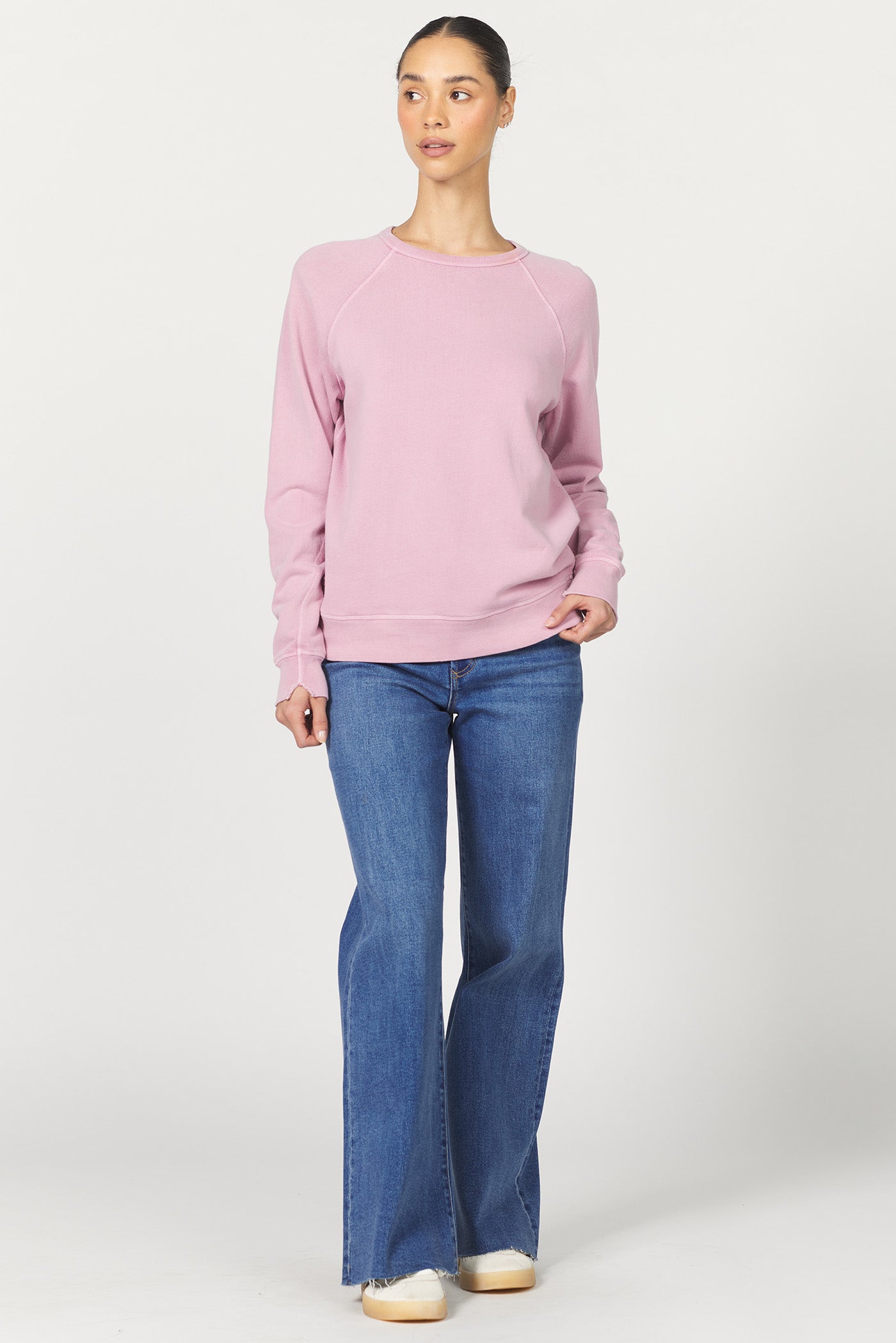 Woman wearing a pink sweatshirt and blue jeans on a white background